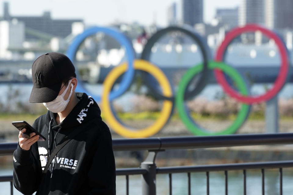 In this March 3, 2020, photo, a tourist wearing a protective mask takes a photo with the Olympic rings in the background, at Tokyo's Odaiba district in Tokyo. Japan's Olympic minister has suggested in Parliament that the Tokyo Olympics might be pushed back a few months from it July 24 opening. The games are under threat from a spreading virus from China that has reached the pandemic stage. But the so-called “Home City Contract”signed by the International Olympic Committee and Japanese officials gives the IOC wide latitude in terminating the Olympics. (AP Photo/Eugene Hoshiko)