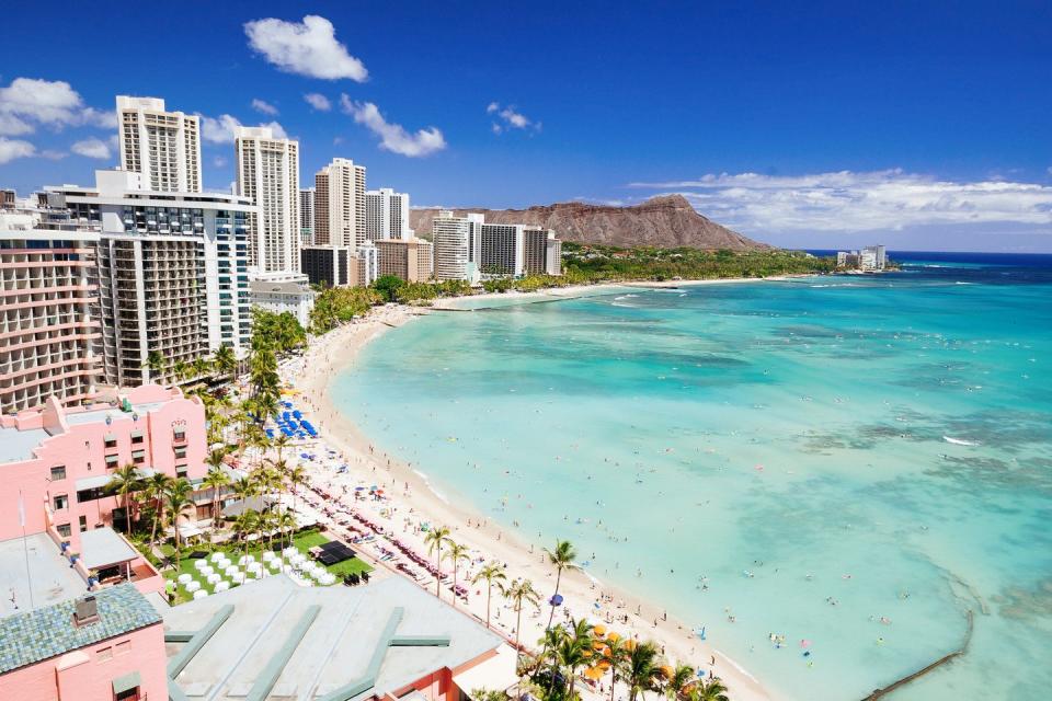 skyline shot of curve of waikiki beach with skyrises, white sand and volcano in background