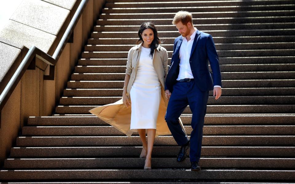 TOPSHOT - Britain's Prince Harry and his wife Meghan walk down the stairs of the iconic Opera House to meet people on October 16, 2018. - Prince Harry and Meghan have made their first appearances since announcing they are expecting a baby, kicking off a high-profile Pacific trip with a photo in front of Sydney's dazzling Opera House and posing with koalas. (Photo by STR / AFP)        (Photo credit should read STR/AFP via Getty Images)