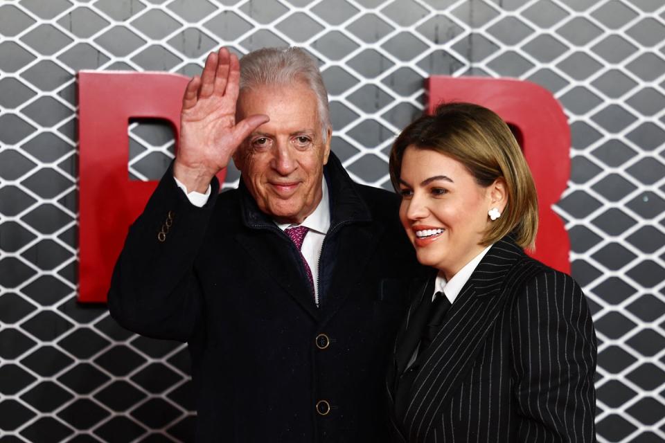 piero ferrari waving and smiling to spectators out of view as romina gingasu smiles and looks left, both wear black jackets and white collared shirts