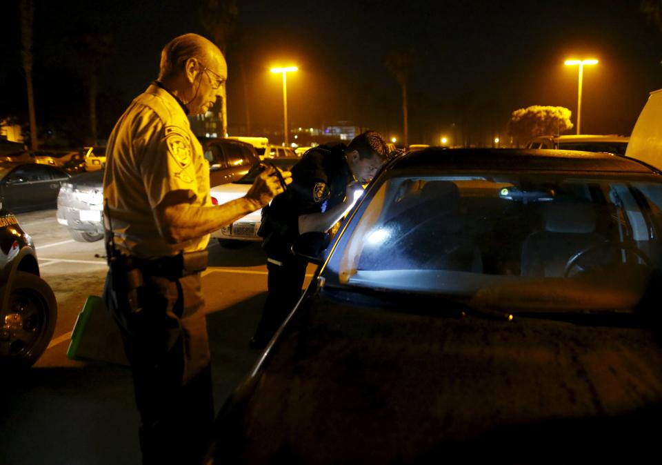 Retired Senior Volunteer Patrol member Henry Miller (L) is assisted by San Diego Police officer Joe Hilton after Miller found a stolen vehicle on his night patrol with partner Steve Rubin in San Diego, California, United States April 30, 2015. (REUTERS/Mike Blake)