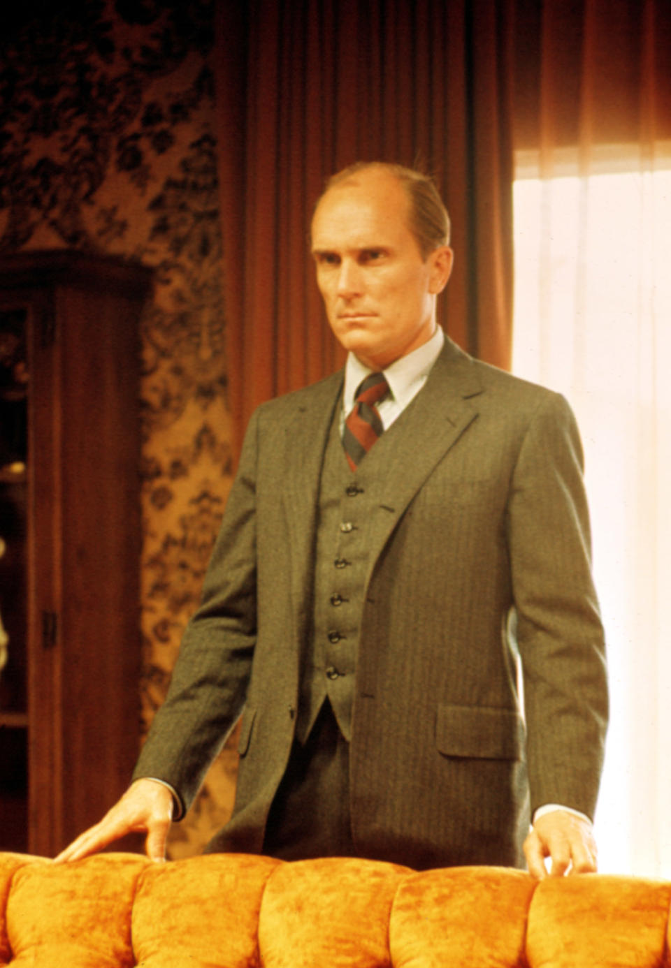 Robert Duvall in a suit, standing behind a chair, from a scene in "The Godfather."