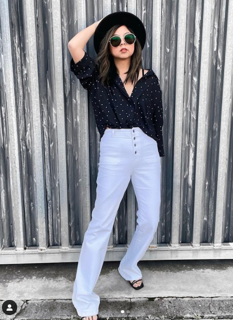 Woman wearing white flared jeans and a black top and hat