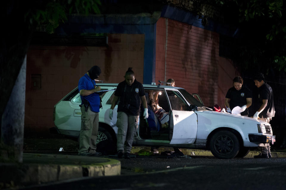FILE - In this Aug. 20, 2018 file photo, forensic investigators examine the crime scene where a man was executed while driving his car, in San Salvador, El Salvador. President Donald Trump said that he is cutting off nearly $500 million in aid to Honduras, Guatemala and El Salvador help reduce immigration. The aid is meant to promote democracy-building, good governance, trade, agriculture, education, health and public safety and law enforcement. Experts say all of those areas play a direct role in whether people feel they can survive in their home country. (AP Photo/Rebecca Blackwell, File)