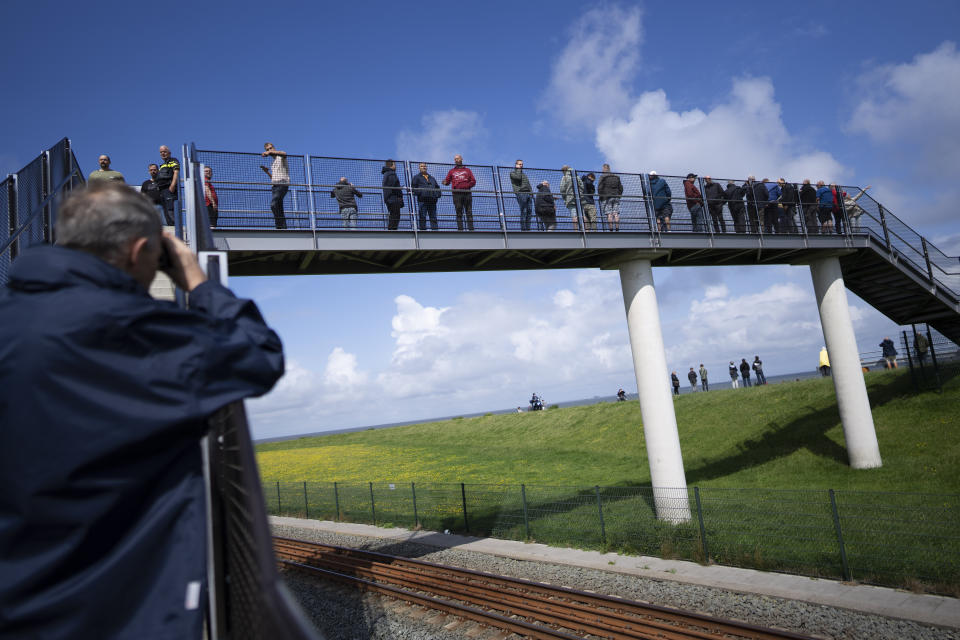 People watch on a bridge a stricken cargo ship Fremantle Highway, that caught fire while transporting thousands of cars from Germany to Singapore, is towed into the port of Eemshaven, the Netherlands, on Thursday, Aug. 3, 2023. The ship that burned for almost a week close to busy North Sea shipping lanes and a world renowned migratory bird habitat will be salvaged at the northern Dutch port. (AP Photo/Peter Dejong)