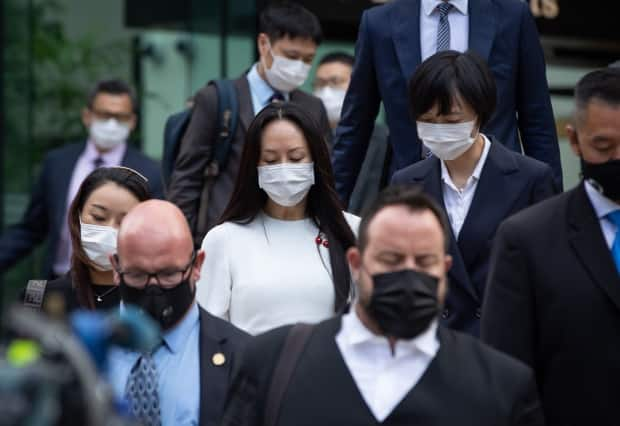 Huawei chief financial officer Meng Wanzhou, (centre in white), is flanked by security guards, Huawei employees and members of her legal team as she exits B.C. Supreme Court on the day her defence made its final submissions.  (Darryl Dyck/Canadian Press - image credit)