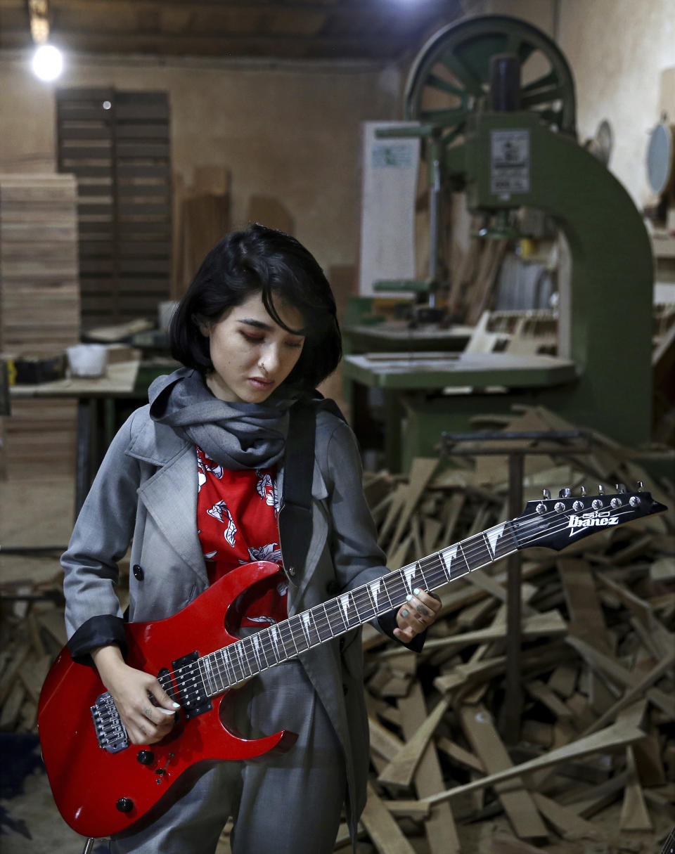 In this July 20, 2018 photo, Afghan musician Soraya Hosseini, a member of the Arikayn rock band, plays guitar at a furniture workshop in Eslamshahr, outside Tehran, Iran. Like others in Iran's vibrant arts scene, Afghan musicians must contend with hard-liners who view Western culture as corrupt and object to women performing in public. (AP Photo/Ebrahim Noroozi)