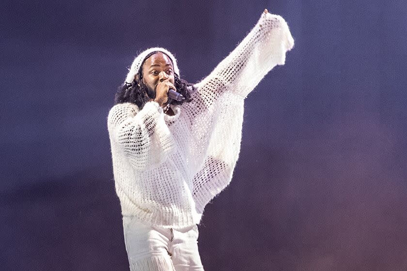 A man in a woven white shirt holds up one arm and sings into a hand-held microphone.