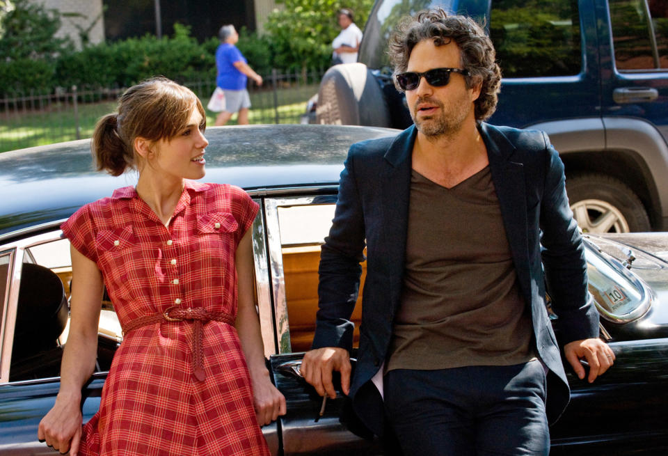 A man and a woman talk while leaning against a car