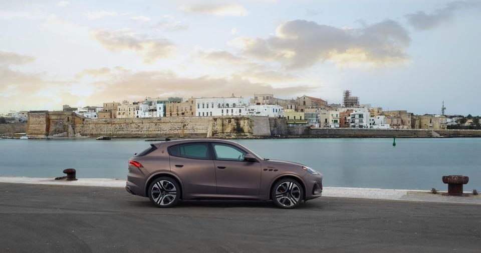 maserati grecale folgore parked on a road by a body of water with buildings in the background