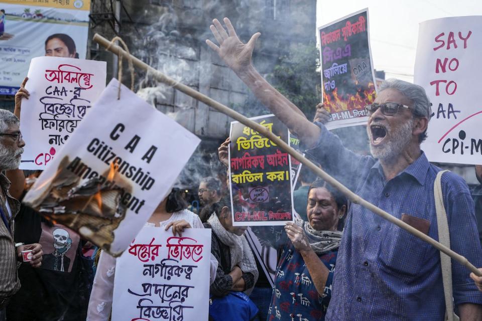 Bearded man shouts and extends his arm. He's surrounded by protesters holding signs.