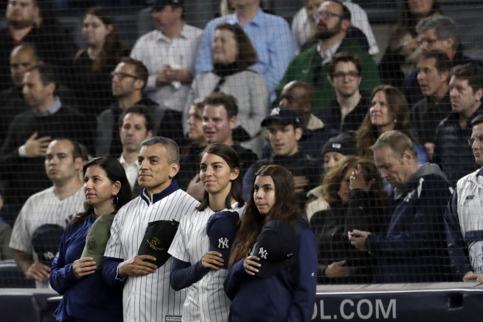 Marine Corps Lt. Col. Manuel Merino, second from left, of New York, who served in Operation Iraqi Freedom, stands with his family as they listen to "God Bless America" during the seventh-inning stretch of a baseball game between the New York Yankees and the Kansas City Royals, Thursday, April 18, 2019, in New York. The Yankees have suspended the use of Kate Smith's recording of "God Bless America" while they investigate an allegation of racism against the singer. The New York Daily News reported there are conflicting claims about Smith's 1939 song "That's Why Darkies Were Born." The song originated in the 1931 Broadway review "George White's Scandals," and was considered satire. It was recorded by Smith and by Paul Robeson, who was black. (AP Photo/Julio Cortez)