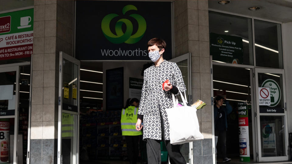 A woman is seen leaving a Woolworths store while wearing a mask