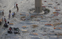 Policemen stand next to the bodies buried in shallow graves on the banks of Ganges river in Prayagraj, India, Saturday, May 15, 2021. Police are reaching out to villagers in northern India to investigate the recovery of bodies buried in shallow sand graves or washing up on the Ganges River banks, prompting speculation on social media that they were the remains of COVID-19 victims. (AP Photo/Rajesh Kumar Singh)