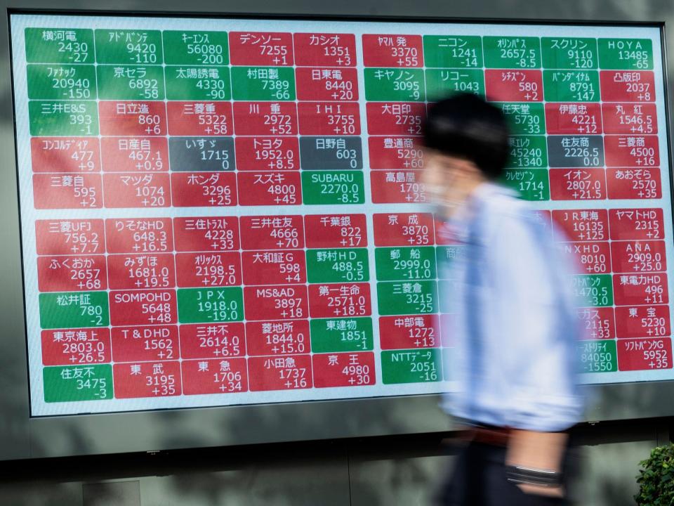 A man walks past an electronic board showing the values of various companies trading on the Tokyo Stock Exchange, along a street in Tokyo on December 7, 2022.