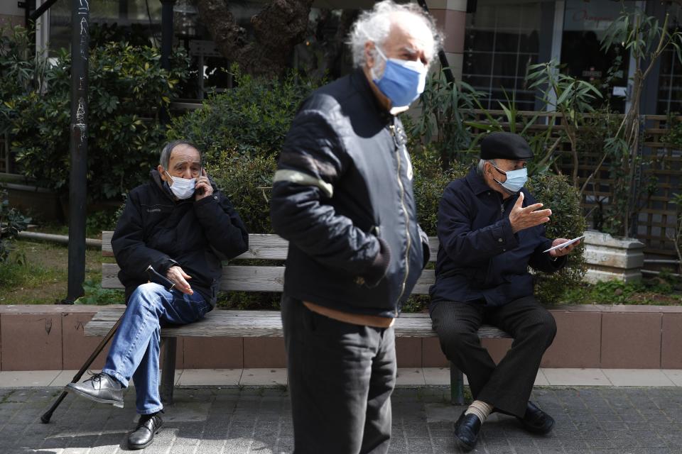 Two elderly men sit on a bench as another one waits in a queue to conduct a rapid test for the COVID-19 in Athens, Wednesday, March 3, 2021. Greece has recorded a new spike in COVID-19 infections, nearly half of which were recorded in the greater Athens region where hospital intensive care units are quickly filling up. (AP Photo/Thanassis Stavrakis)