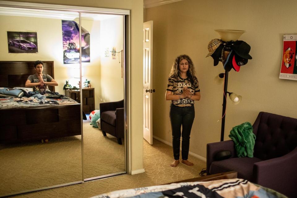 Shashi Singh stands in a bedroom praying while a mirror shows her son in bed praying