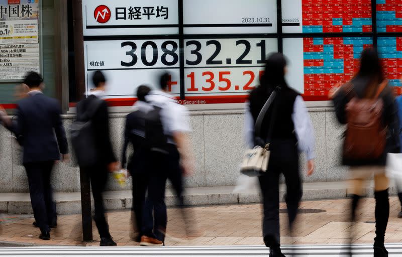 Pedestrians walk past an electronic board displaying Nikkei share average, outside a brokerage in Tokyo