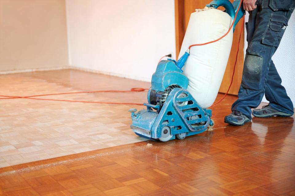 Worker polishing parquet floor with grinding machine