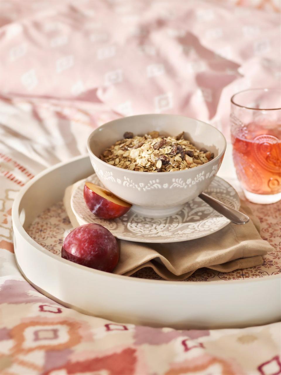 ikat bedding on bed with circular patterned tray set with a bowl of muesli and a juice