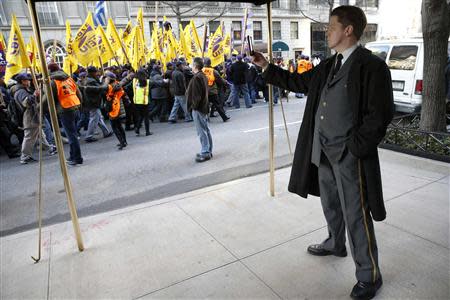 A doorman takes pictures with a mobile phone as members of the Service Employees International Union (SEIU) march past in a protest in support of a new contract for apartment building workers in New York City, April 2, 2014. REUTERS/Mike Segar