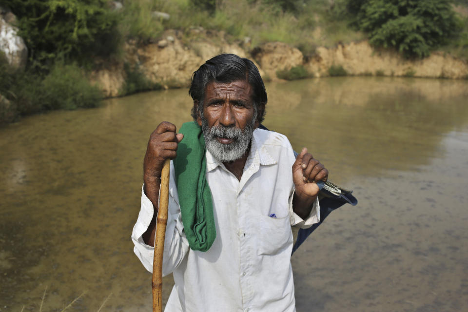 Kalmane Kamegowda, a 72-year-old shepherd, poses for a photo in front of one of the 16 ponds he created at a hillock near Dasanadoddi village, 120 kilometers (75 miles) west of Bengaluru, India, Wednesday, Nov. 25, 2020. Kamegowda, who never attended school, says he's spent at least $14,000 from his and his son’s earnings, mainly through selling sheep he tended over the years, to dig a chain of 16 ponds on a picturesque hill near his village. (AP Photo/Aijaz Rahi)