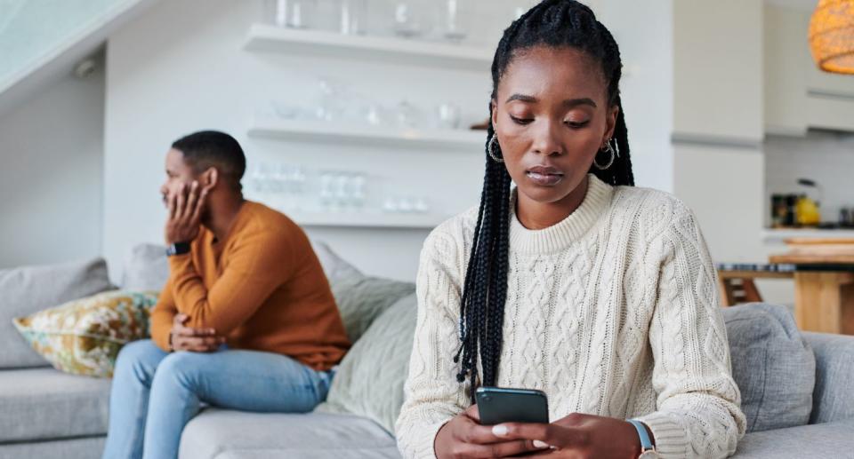 Man and woman sit on opposite ends of the couch with woman on phone