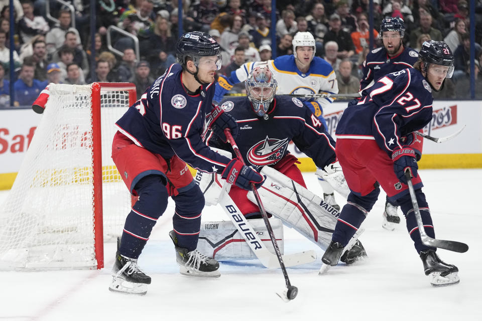 Columbus Blue Jackets center Jack Roslovic (96) clears the puck from in front of goaltender Daniil Tarasov, center, during the first period of the team's NHL hockey game against the Buffalo Sabres, Friday, Feb. 23, 2024, in Columbus, Ohio. (AP Photo/Sue Ogrocki)