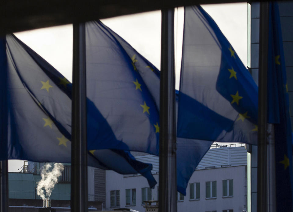 Smoke rises from a chimney behind EU flags fluttering in the wind outside EU headquarters in Brussels, Thursday, Dec. 24, 2020. European Union and British negotiators worked through the night and into Christmas Eve in the hopes of putting the finishing touches on a trade deal that should avert a chaotic economic break between the two sides on New Year's Day. (AP Photo/Virginia Mayo)