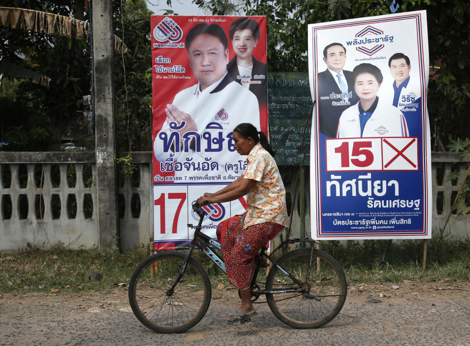 In this March 14, 2019, photo, a Thai woman on a bicycle moves past the posters of Pheu Chart party's Veerawit Chuajunud, left, who changed his name to Thaksin Chuajunud, and Pracha Pracharat Party's candidate and Prime Minister Prayuth Chan-ocha, left on right poster, during an election campaign in Nakhon Ratchasima, Thailand. Thailand’s former Prime Minister Thaksin Shinawatra is in exile and banned from interfering in the country’s politics. But his name is a powerful political attraction and in tribute, and to win votes, some candidates in general election on Sunday, March 24, 2019 have changed their names to Thaksin so supporters of the former leader can register their loyalty at the ballot box. (AP Photo/Sakchai Lalit)