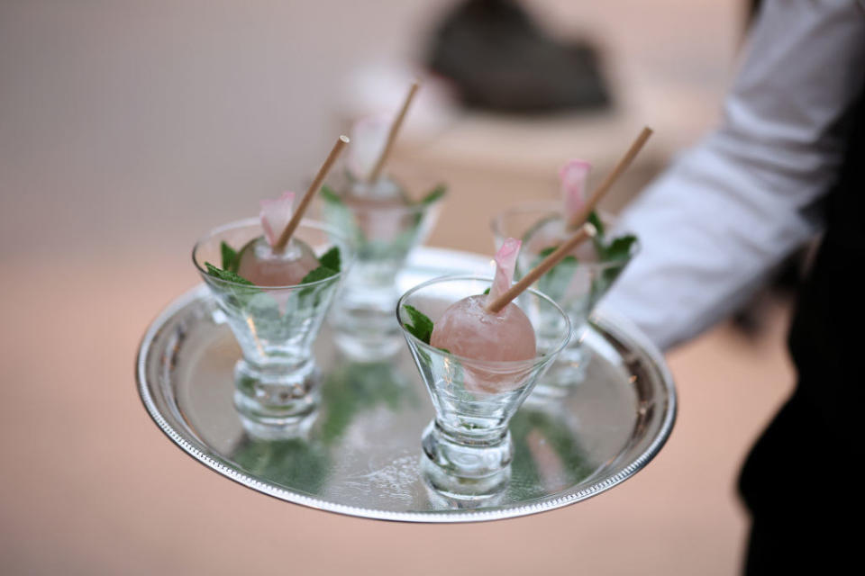 A waiter holds a tray with four small glasses with a jelly like ball inside