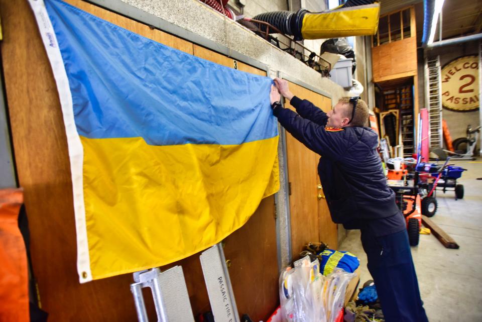 Firefighter Scott Hoitsma of Station 4 in Clifton, puts a Ukrainian flag on the wall as personal protective equipment including air tanks, masks, gloves and turnout coats that will be donated to Ukraine, gather in front of the flag at Eastside Fire House in Passaic on Thursday, March 3, 2022.