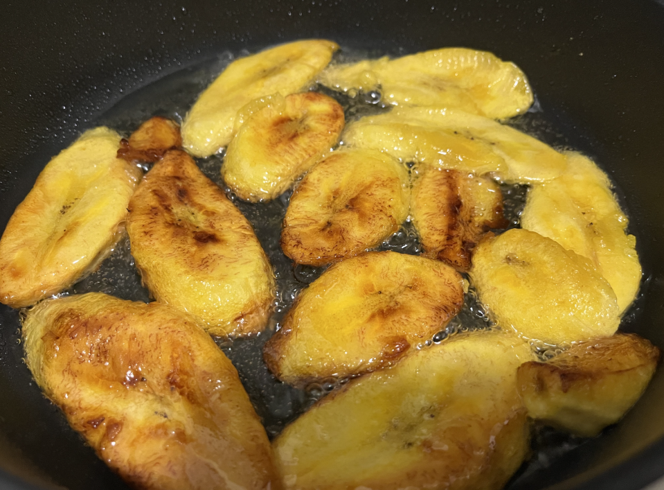 Plantains frying in a pan with vegetable oil.