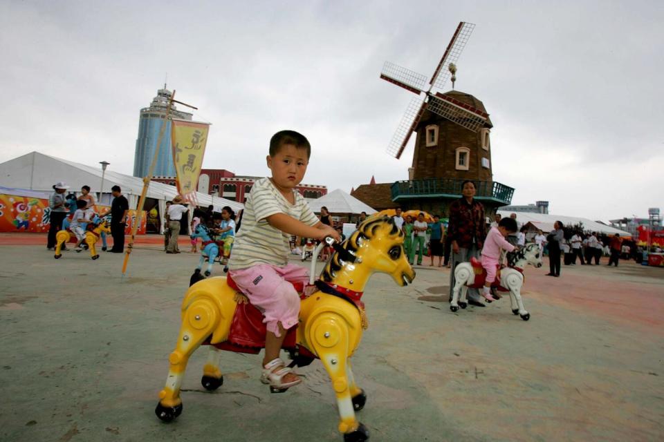 A child rides a yellow toy pony at a park with a windmill