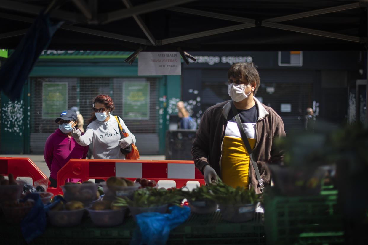 Shoppers wearing protective face masks at a fruit and vegetable market stall in East Ham, east London, as the UK continues in lockdown to help curb the spread of the coronavirus. (Photo by Victoria Jones/PA Images via Getty Images)