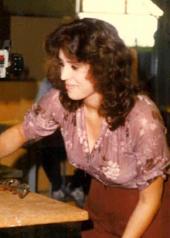 An older image of a smiling woman with curly brown hair, wearing a pink floral blouse.