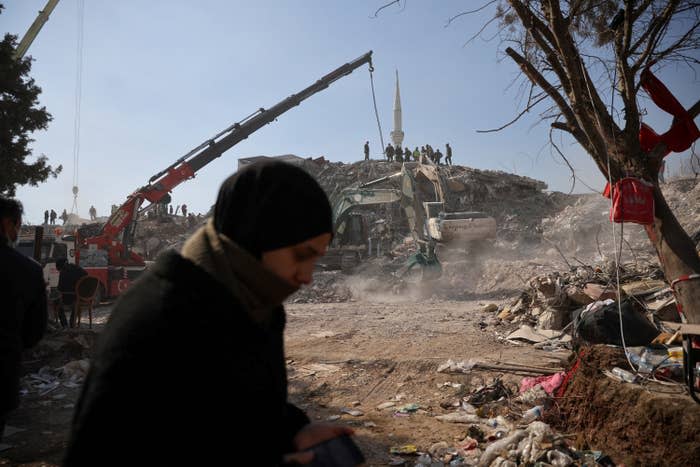 People stand amid rubble at the site of a collapsed building as the search for survivors continues in the aftermath of a deadly earthquake in Kahramanmaras, Turkey, on Feb. 12, 2023. 