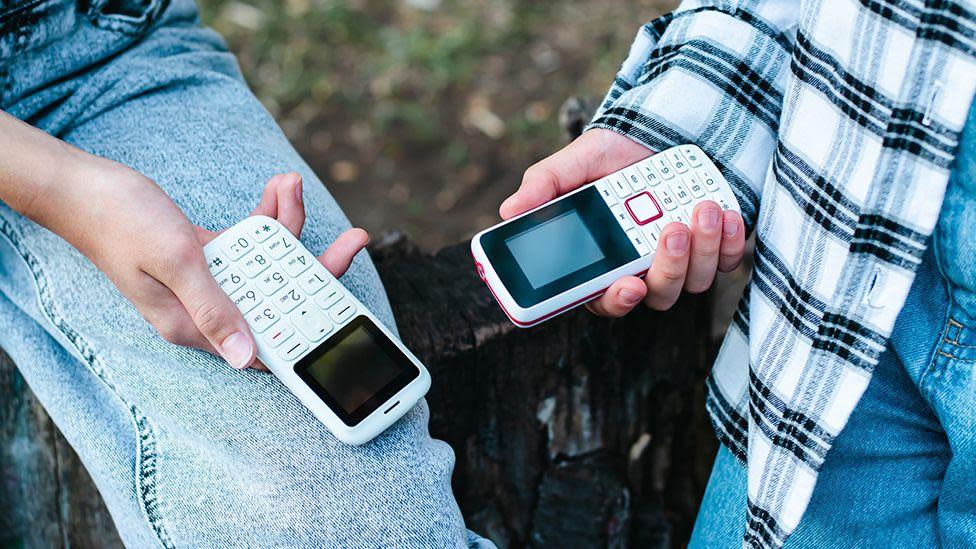 Small push-button mobile phones pictured in the hands of teenagers outdoors