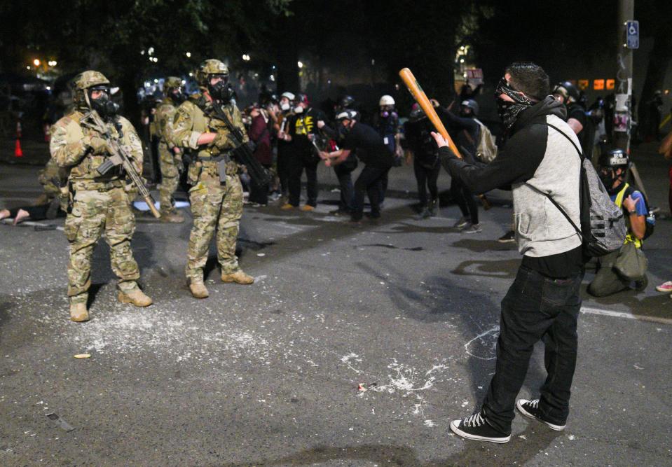 A man upset about federal agents detaining protesters threatens them with a baseball bat and dares them to shoot him during a protest outside the federal courthouse in Portland, Ore., early on July 27, 2020.