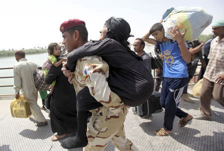 A member of Iraqi security forces carries an elderly woman across a bridge on the outskirts of Baghdad, May 24, 2015. REUTERS/Stringer