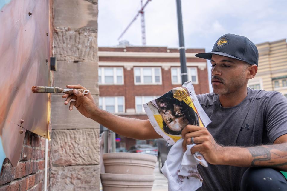 Elio Mercado paints a mural of Etheridge Knight referencing a digital illustration he created Thursday, June 22, 2023, in Indianapolis.