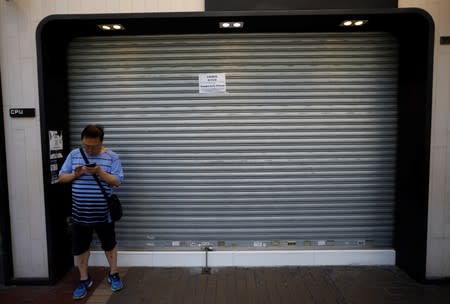 A man stands in front of a shop, with a notice on its shutters announcing it is closed for the day due to traffic disruptions, during a general strike in Hong Kong