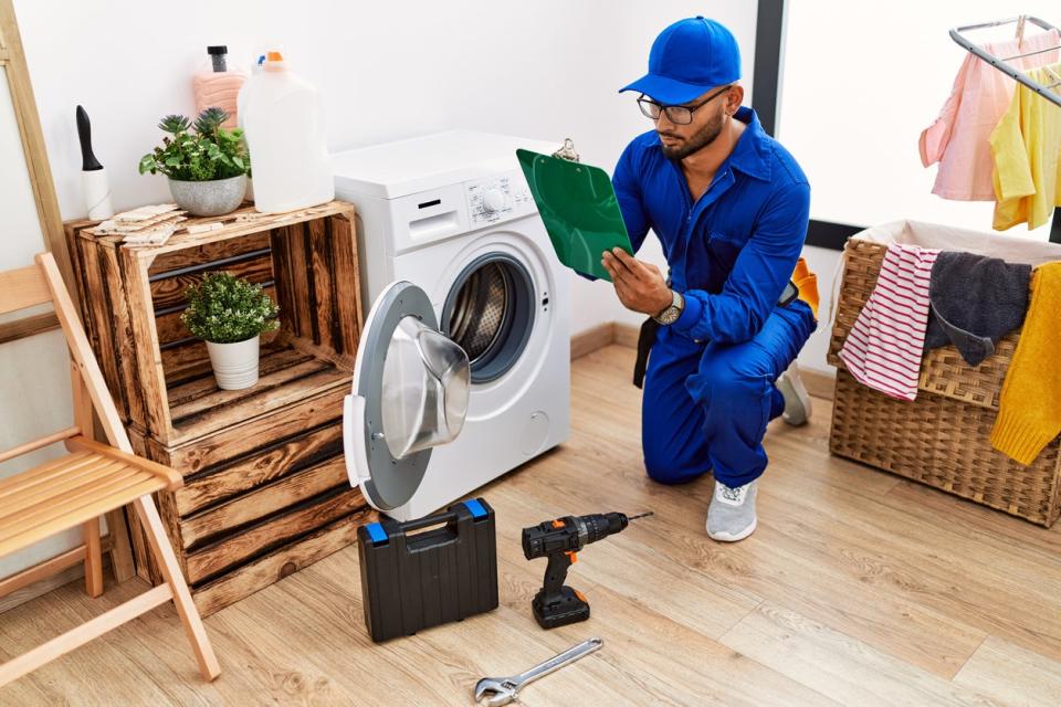  Young arab man wearing technician uniform writing on clipboard at laundry room