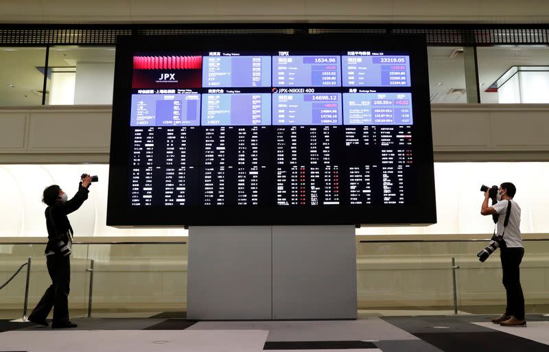 Photographers take photos near a large screen showing stock prices at the Tokyo Stock Exchange after market opens in Tokyo