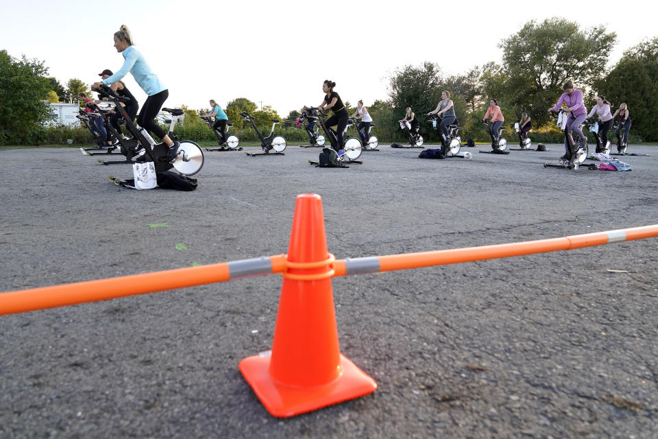 Jackie Brennan, of Merrimac, Mass., front left, pedals with others on stationary exercise bikes during a spinning class in a parking lot outside Fuel Training Studio, Monday, Sept. 21, 2020, in Newburyport. The gym's revenue is down about 60% during the COVID-19 pandemic. Fuel Training Studio plans to continue holding outdoor classes into the winter with the help of a planned greenhouse-like structure with heaters but no walls. (AP Photo/Steven Senne)