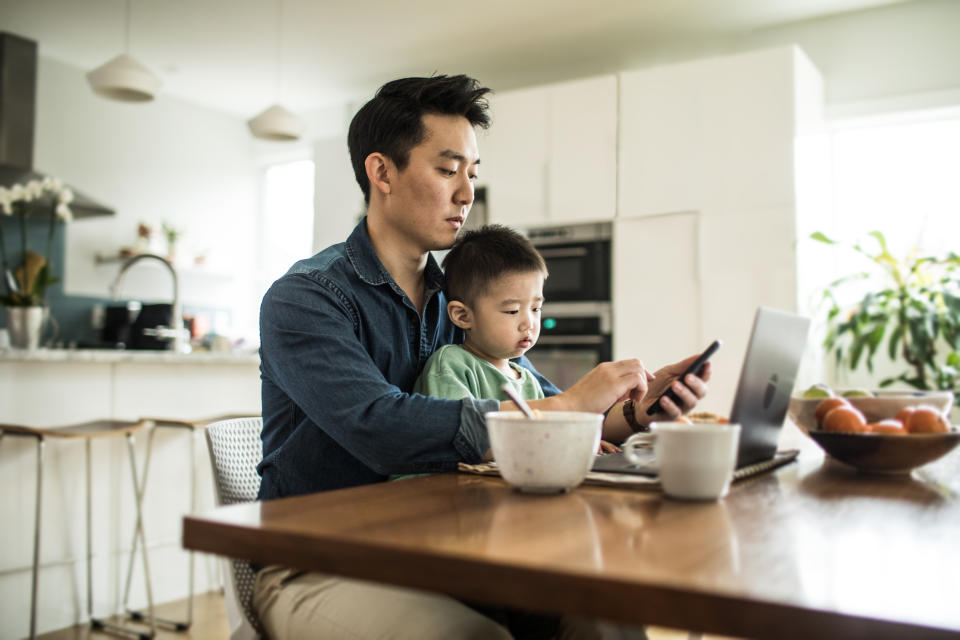 Father multi-tasking with young son (2 yrs) at kitchen table