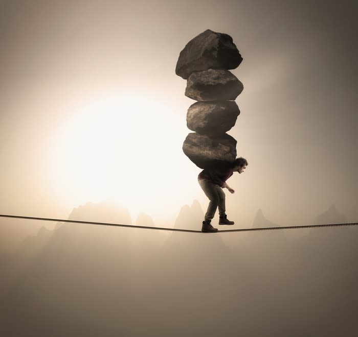 Man walking tightrope carrying four boulders on his back