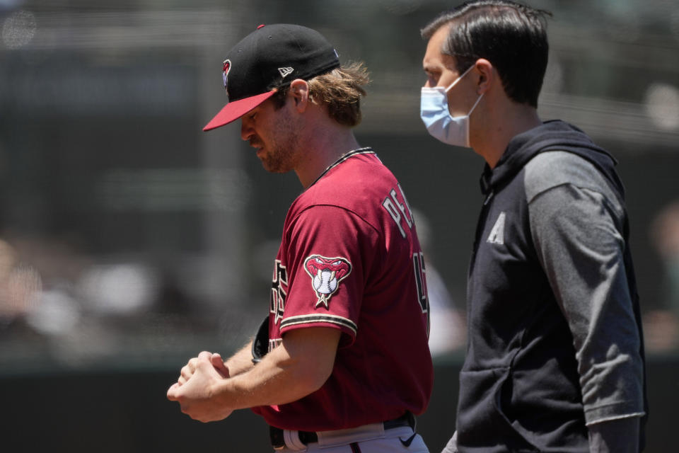 Arizona Diamondbacks pitcher Matt Peacock, left, leaves the game against the Oakland Athletics with an injury to his throwing hand during the second inning of a baseball game Wednesday, June 9, 2021, in Oakland, Calif. (AP Photo/Tony Avelar)