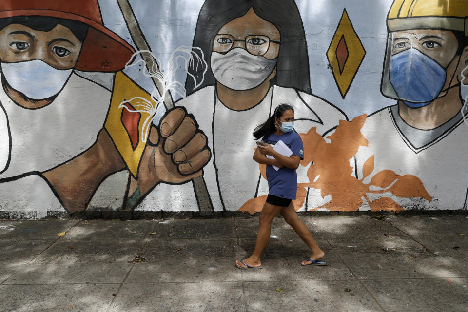 A woman wearing protective mask to prevent the spread of the coronavirus walk past a mural showing frontliners in Manila, Philippines on Wednesday, Oct. 21, 2020. The Philippines lifted a ban on non-essential foreign trips by Filipinos Wednesday but the immigration bureau said the move did not immediately spark large numbers of departures for tourism and leisure. (AP Photo/Aaron Favila)