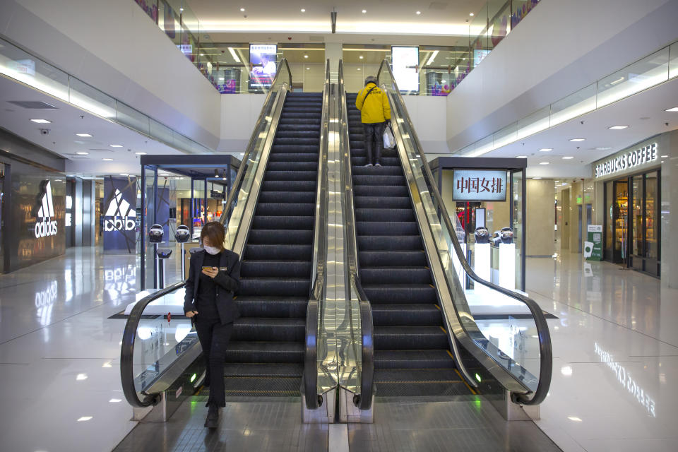 In this Tuesday, Jan. 28, 2020 photo, a shop worker and a deliveryman ride an escalator at a nearly empty shopping mall in Beijing. Fears of a virus outbreak have kept many indoors and at home in China's capital. Cultural landmarks such as the Great Wall and Forbidden City have closed their doors to visitors, nearly deserted shopping malls have reduced their operating hours, and restaurants that remain open draw just a handful of customers. (AP Photo/Mark Schiefelbein)